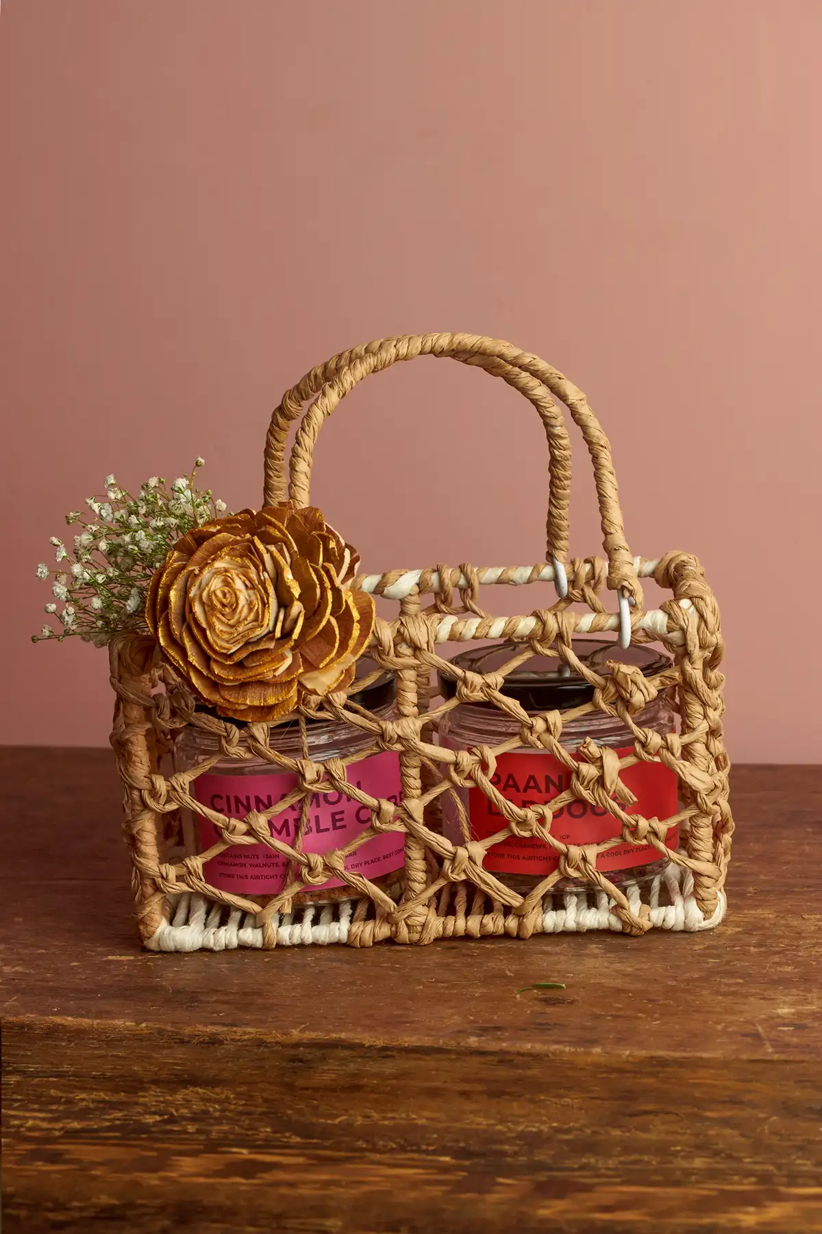 Choti Diwali Basket 1 A small woven basket with two glass jars inside, decorated with a wooden flower and a sprig of babys breath.