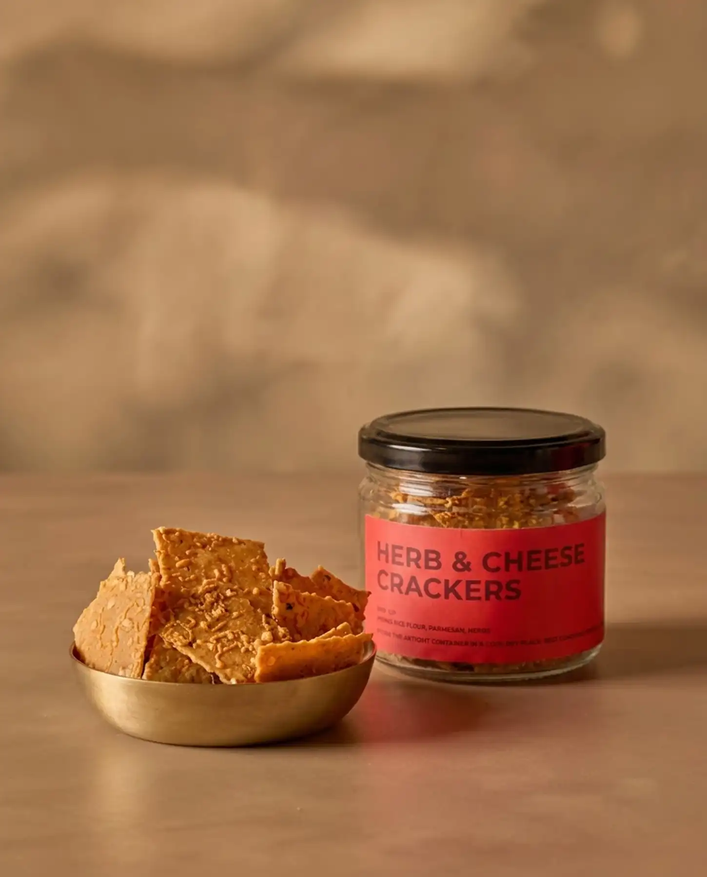 Choti Diwali Basket 4 A metal bowl filled with Herb & Cheese crackers next to a glass jar with a red label reading Herb & Cheese Crackers.