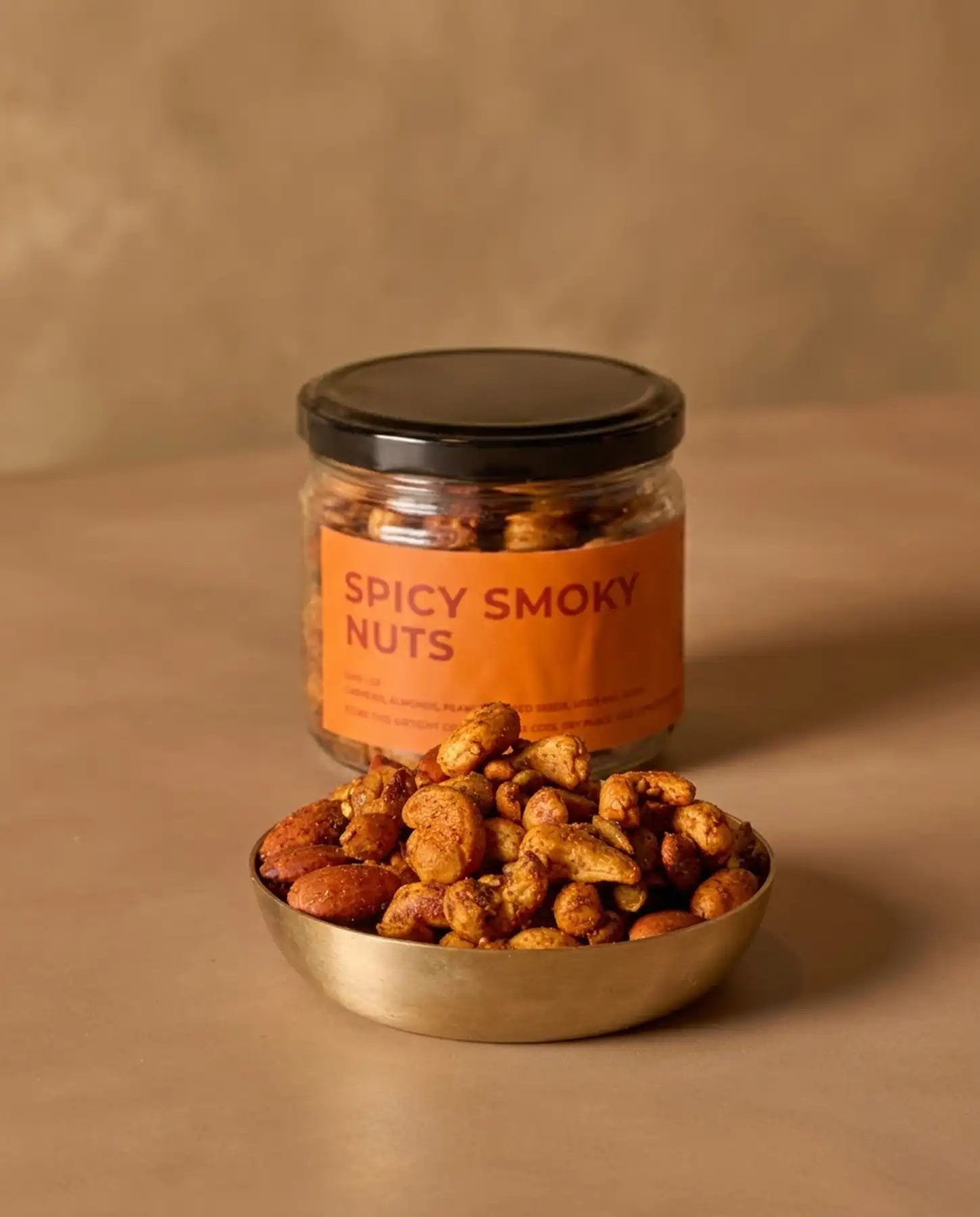 Choti Diwali Basket 5 A metal bowl filled with spiced nuts from a Choti Diwali Basket sits in front of a glass jar labeled Spicy Smoky Nuts.